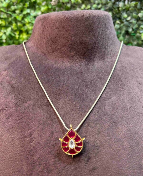 The image shows a close-up of a delicate necklace with a pendant. The pendant is the focal point of the image. It has a crescent moon shape. The moon is adorned with intricate Kundan work, featuring small, colorful gemstones. The overall color scheme seems to be a combination of gold and silver.