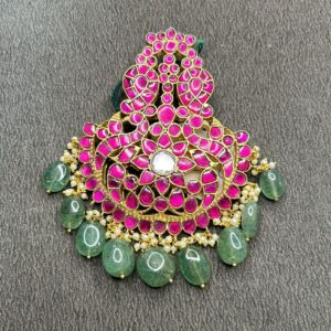"A close-up of a traditional Indian Kundan pendant with pink stones, pearls, and green beads."