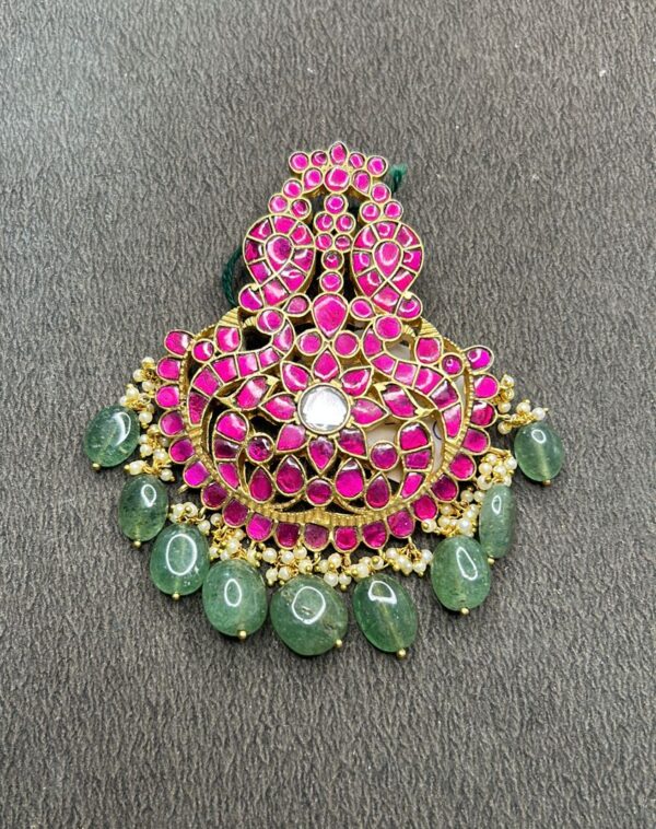 "A close-up of a traditional Indian Kundan pendant with pink stones, pearls, and green beads."