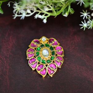 "A close-up of a gold Kundan pendant with rubies, emeralds, and a pearl."
