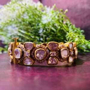 The image shows a pair of elegant bangles adorned with a cluster of sparkling Moissanite stones. The bangles are crafted from 925 sterling silver, giving them a lustrous and refined appearance. The design features a delicate floral motif, adding a touch of intricate detail