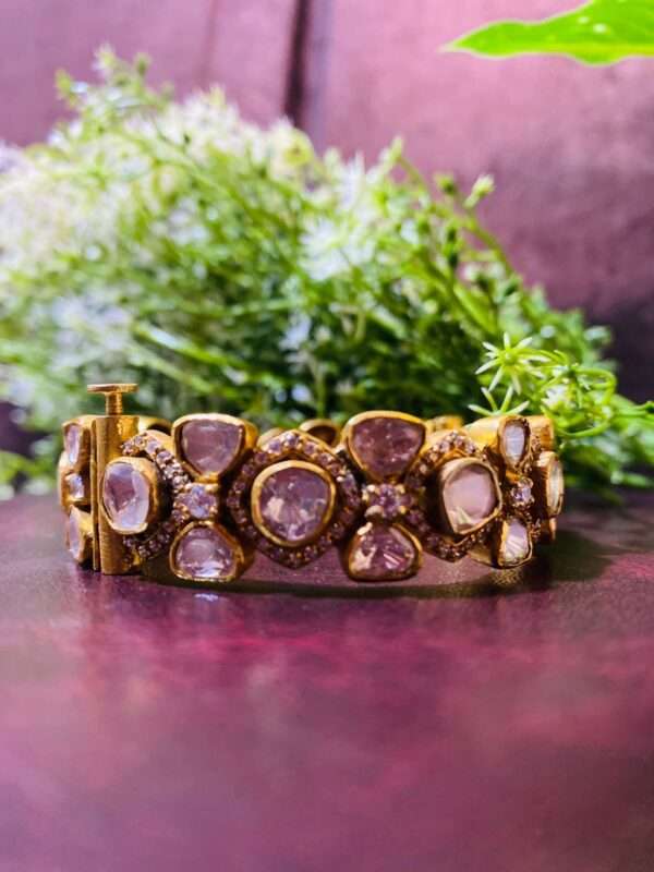 The image shows a pair of elegant bangles adorned with a cluster of sparkling Moissanite stones. The bangles are crafted from 925 sterling silver, giving them a lustrous and refined appearance. The design features a delicate floral motif, adding a touch of intricate detail