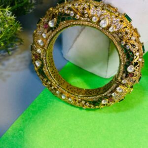 The craftsmanship of the bangles appears to be intricate, with detailed patterns and settings for the gemstones. The colors of the gemstones create a vibrant and eye-catching contrast against the gold tone of the bangles. The image is well-lit and showcases the details of the bangles clearly.