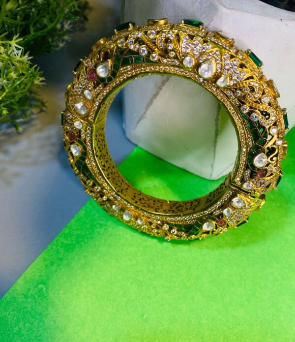 The craftsmanship of the bangles appears to be intricate, with detailed patterns and settings for the gemstones. The colors of the gemstones create a vibrant and eye-catching contrast against the gold tone of the bangles. The image is well-lit and showcases the details of the bangles clearly.