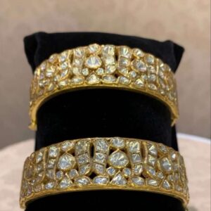 The image shows a pair of stunning gold bangles adorned with what appears to be moissanite stones. The bangles have a classic design with multiple rows of pave-set moissanite, creating a dazzling and luxurious look. Moissanite is a synthetic gemstone that closely resembles diamonds in appearance, but is much more affordable.