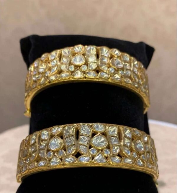 The image shows a pair of stunning gold bangles adorned with what appears to be moissanite stones. The bangles have a classic design with multiple rows of pave-set moissanite, creating a dazzling and luxurious look. Moissanite is a synthetic gemstone that closely resembles diamonds in appearance, but is much more affordable.