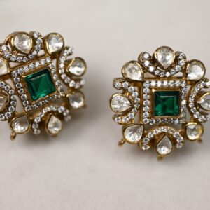 The image shows a pair of stunning earrings. They are made of gold and feature a square-shaped emerald gemstone in the center. The emerald is surrounded by a delicate floral design composed of small white stones, likely diamonds or moissanites. The earrings have a vintage or antique look and are sure to make a statement.