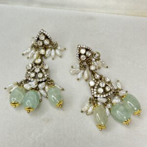 The image shows a pair of elegant and luxurious earrings. They have a multi-tiered design with each tier showcasing sparkling moissanites. The earrings are further embellished with delicate pearls and a cluster of beautiful green stones, adding a touch of color and contrast. The intricate craftsmanship and attention to detail make these earrings a true masterpiece. They would be perfect for special occasions or to add a touch of glamour to any outfit.
