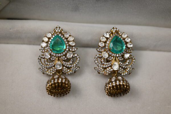 The image features a pair of stunning green moissanite earrings. The earrings are crafted in silver and feature a teardrop-shaped design with intricate floral detailing. The teardrop drops are adorned with multiple facets that reflect light beautifully, creating a dazzling sparkle.