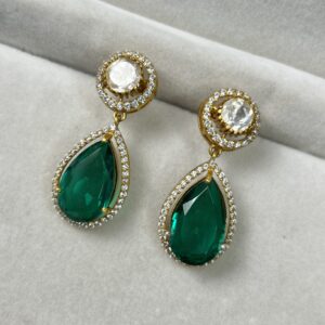 The image shows a pair of elegant earrings on a white surface. The earrings are made of gold and feature a combination of green and white gemstones. Each earring has a teardrop-shaped green stone, surrounded by a halo of smaller white stones. Above the green stone, there is a circular cluster of white stones.