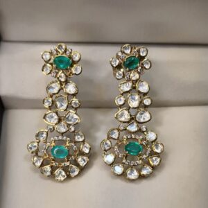 The image shows a pair of stunning dangle earrings. The earrings are made of gold and feature a cluster of round-cut diamonds and emeralds. The emeralds are a vibrant green and the diamonds sparkle brightly.