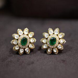 "Close-up of a pair of elegant gold stud earrings with a delicate floral design. Each earring is adorned with a cluster of sparkling moissanites surrounding a captivating emerald-cut green gemstone."