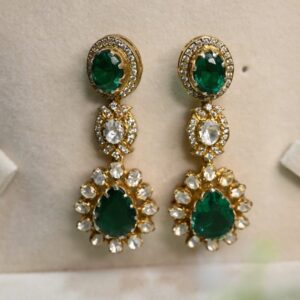 The image shows a pair of elegant drop earrings. They appear to be made of gold and feature a combination of gemstones. There are round, faceted diamonds, possibly white or colorless, and a larger, oval-shaped green stone, which could be an emerald or another green gemstone. The earrings have a delicate, elongated design with multiple drops or pendants, creating a graceful and eye-catching look.
