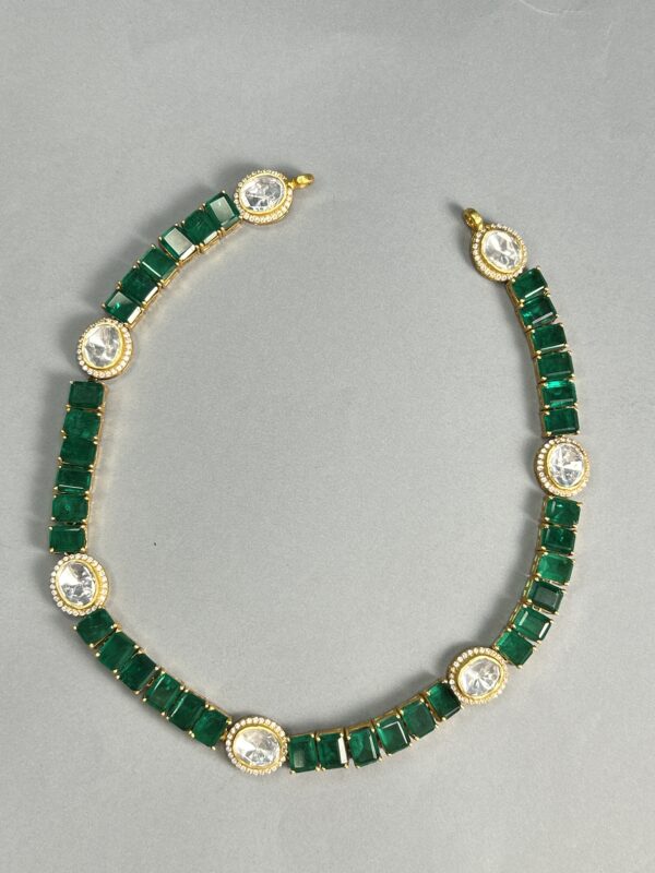 The image you sent shows a necklace made with a combination of emerald-cut and round-cut moissanites. The necklace appears to be a choker style, sitting close to the neck. The moissanites are set in a gold-plated setting, creating a luxurious and warm look. The overall design is minimalist and elegant, with clean lines and simple geometric shapes.