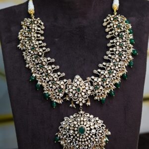 The image showcases a stunning necklace adorned with a multitude of sparkling gemstones. The central motif appears to be a large, circular pendant embellished with a cluster of what looks like diamonds or possibly moissanites. This central piece is surrounded by a delicate floral pattern that extends outwards, forming a wide, collar-like necklace. The design is further embellished with additional gemstones of varying sizes, creating a luxurious and opulent look. The necklace rests on a dark, velvet-like surface, possibly a display mannequin.