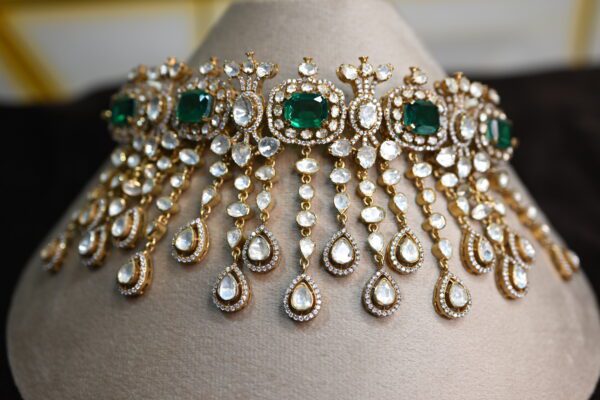 The image showcases a beautiful necklace crafted with moissanites. The necklace features a central cluster of emerald-cut moissanites, surrounded by a halo of smaller, pear-shaped moissanites. Delicate chains of teardrop-shaped moissanites cascade downwards from the central cluster, creating a mesmerizing waterfall effect. The overall design is reminiscent of traditional Indian jewelry with a contemporary touch. 925 Silver