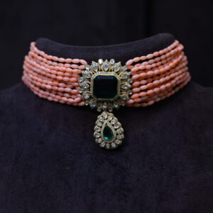 The image showcases a beautiful necklace. It appears to be a choker style, with multiple strands of coral beads creating a layered effect. A large, emerald-cut moissanite gemstone is the centerpiece, surrounded by smaller diamonds. The necklace is set in a gold-plated frame, adding to its luxurious look. Sparkling Moissanite Choker Necklace