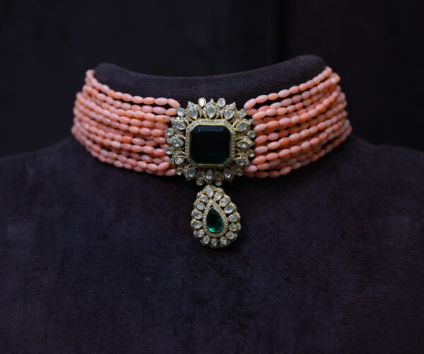 The image showcases a beautiful necklace. It appears to be a choker style, with multiple strands of coral beads creating a layered effect. A large, emerald-cut moissanite gemstone is the centerpiece, surrounded by smaller diamonds. The necklace is set in a gold-plated frame, adding to its luxurious look. Sparkling Moissanite Choker Necklace