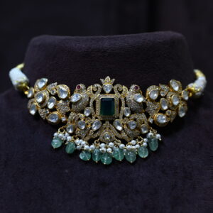 The image shows a necklace on a black velvet stand. The necklace has a central large emerald-cut green gemstone surrounded by smaller white gemstones and pearls. The design appears to be inspired by nature, with intricate floral and leaf motifs. The overall effect is one of luxury and elegance.