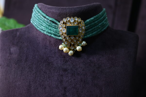 The image you sent shows a beautiful necklace with a central emerald gemstone and a halo of sparkling moissanites. The necklace also features a delicate floral design and a row of pearls, creating a truly unique and captivating look.