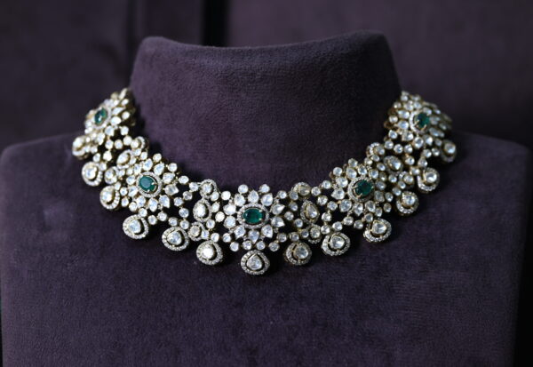 The image showcases a stunning necklace adorned with a cluster of large, faceted gemstones. The necklace appears to be resting on a dark, velvety surface, possibly a jewelry display. The background is blurred, drawing attention to the intricate details of the necklace. Premium Moissanite Choker Necklace