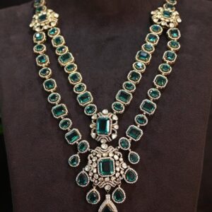 The image shows a beautiful necklace with a double-layered design. It's adorned with numerous emerald-cut moissanites, which are known for their exceptional brilliance and fire. The stones are set in a delicate gold frame, creating a luxurious and sophisticated look. The necklace features a central pendant with a larger moissanite surrounded by smaller stones. The pendant is connected to the double-layered chain, which is also adorned with emerald-cut moissanites throughout.