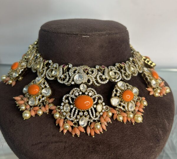 The image showcases a beautiful necklace adorned with a cluster of orange gemstones and sparkling white stones. The necklace appears to be a choker style, sitting close to the neck. The central design features three large, round orange gemstones, likely coral or carnelian, surrounded by a delicate filigree pattern. Smaller white stones, possibly diamonds or moissanite, are interspersed throughout the design, adding to its brilliance. The necklace is displayed on a brown mannequin neck, highlighting its intricate details. 925 Silver