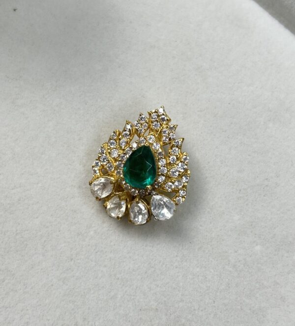 "Gold-toned pendant featuring a pear-shaped green gemstone surrounded by clear teardrop and round-cut stones in an intricate design, displayed on a light background."