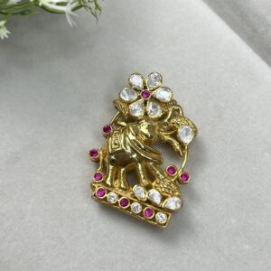 The image showcases a stunning pendant featuring an elephant motif. The elephant, a symbol of wisdom and strength, is intricately crafted and appears to be made of gold. It is adorned with a floral design and studded with sparkling moissanite stones, adding a touch of brilliance and elegance. The pendant rests on a soft, white surface with a few delicate white flowers nearby, creating a visually appealing backdrop.
