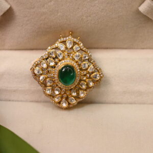 The image shows a beautiful pendant featuring a vibrant green moissanite gemstone. The stone is set in a delicate gold-tone mount and surrounded by a halo of smaller moissanite stones. The overall design of the pendant has a classic floral motif. The pendant is displayed in a jewelry box, with a red tulip placed beside it. The contrast of the green stone against the gold and the red flower creates a visually appealing composition.