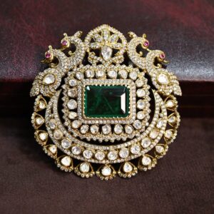 The image shows a close-up of a beautiful jewelry pendant. The pendant is circular in shape and is adorned with a large, square-cut emerald moissanite stone in the center. The emerald moissanite is surrounded by a halo of smaller, round-cut moissanite stones. The pendant also features intricate filigree work and two delicate peacock motifs on either side, adding a touch of elegance and whimsy to the design. The pendant appears to be set in gold.