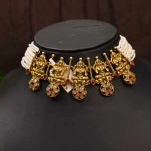 The image shows a beautiful temple necklace adorned with intricate details and sparkling gemstones. It appears to be made of 925 sterling silver and features a design inspired by Hindu deities, possibly depicting Lord Ganesha. The necklace rests on a black mannequin, showcasing its elegance and craftsmanship. The image also includes a glimpse of a green leaf, adding a touch of nature to the scene.
