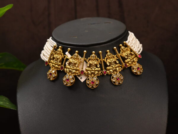 The image shows a beautiful temple necklace adorned with intricate details and sparkling gemstones. It appears to be made of 925 sterling silver and features a design inspired by Hindu deities, possibly depicting Lord Ganesha. The necklace rests on a black mannequin, showcasing its elegance and craftsmanship. The image also includes a glimpse of a green leaf, adding a touch of nature to the scene.