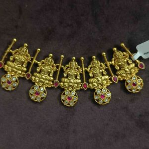 The image shows a beautiful necklace with a temple design. It appears to be made of gold and is adorned with intricate carvings and colorful gemstones. The central motif seems to depict a Hindu deity, possibly Lakshmi or Saraswati. The necklace has a rich and ornate look, suggesting it's a piece of traditional Indian jewelry.