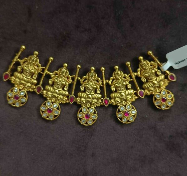 The image shows a beautiful necklace with a temple design. It appears to be made of gold and is adorned with intricate carvings and colorful gemstones. The central motif seems to depict a Hindu deity, possibly Lakshmi or Saraswati. The necklace has a rich and ornate look, suggesting it's a piece of traditional Indian jewelry.