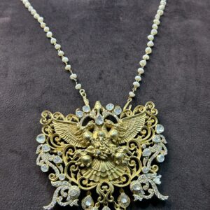 The image you shared is a close-up of a gold pendant depicting a Hindu deity. The pendant is intricately crafted with delicate details and features a combination of gold and pearls. The deity is shown with multiple arms, each holding a different symbol or weapon. The pendant is suspended from a gold chain.