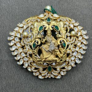 The image shows a beautiful and ornate pendant. It appears to be made of gold and is heavily embellished with sparkling stones, likely diamonds or cubic zirconia. The central design features a depiction of a Hindu deity, possibly Lord Krishna or Vishnu, riding a mythical creature. The pendant is surrounded by intricate floral and geometric patterns, creating a sense of grandeur and opulence.