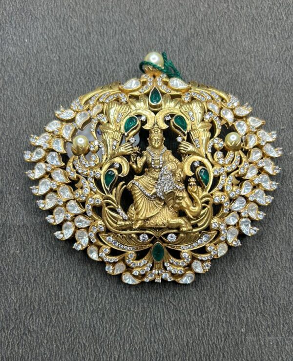 The image shows a beautiful and ornate pendant. It appears to be made of gold and is heavily embellished with sparkling stones, likely diamonds or cubic zirconia. The central design features a depiction of a Hindu deity, possibly Lord Krishna or Vishnu, riding a mythical creature. The pendant is surrounded by intricate floral and geometric patterns, creating a sense of grandeur and opulence.