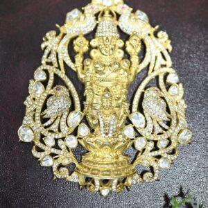 The image shows a beautiful, intricately designed temple pendant. The pendant appears to be made of gold or gold-plated metal and is adorned with sparkling stones, possibly diamonds or cubic zirconia. It features a central figure of a Hindu deity, likely Goddess Lakshmi or Vishnu, seated on a throne. The deity is surrounded by delicate floral motifs and intricate patterns, creating a visually stunning and spiritually significant piece of jewelry.