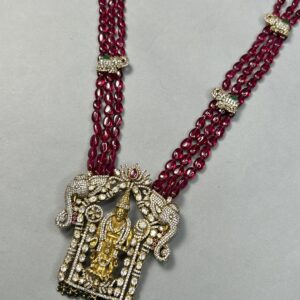 A close-up of a gold necklace with a central temple pendant adorned with red and white gemstones. The pendant depicts a Hindu deity within a temple structure.