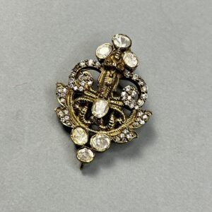 The image shows a close-up of a delicate gold-toned pendant. The pendant appears to be intricately designed with a central motif resembling a temple or a shrine. The design is embellished with numerous small, sparkling stones, likely cubic zirconia, which add to its overall elegance. The pendant hangs from a thin gold-toned chain, which is not fully visible in the image.