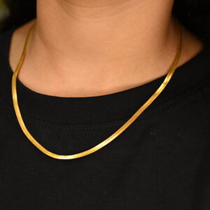 This image shows a close-up of a person wearing a simple yet elegant gold-plated chain necklace. The necklace has a flat, smooth, and shiny design, laying neatly against a black t-shirt. The warm gold tone contrasts beautifully with the black fabric, highlighting the necklace's sleek and polished appearance. The focus is on the neck and necklace, with no visible facial features, emphasizing the jewelry as the main subject.