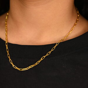 A close-up shot shows a delicate, minimalist necklace made of solid gold links resting on a person's neck wearing a plain black t-shirt. The necklace is the clear focal point, highlighting its simple yet elegant design.