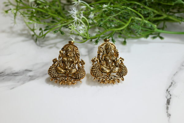 Pair of 925 silver temple earrings featuring a seated deity flanked by peacocks, adorned with ruby-green spinels and antique gold polish."​ This description is concise, informative, and adheres to best practices for accessibility and SEO. If you have multiple images of the earrings from different angles or contexts, consider specifying the view in each alt text, such as "Side view of 925 silver temple earring with deity and peacock design.