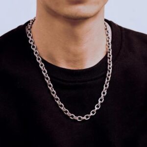 This image shows a close-up of a person wearing a thick, silver chain necklace over a plain black crew-neck shirt. The necklace features large, oval-shaped links with a polished, metallic finish, giving it a bold, stylish, and urban look. The background is simple and light, keeping the focus on the necklace and the outfit. The overall vibe is modern, minimalistic, and streetwear-inspired.