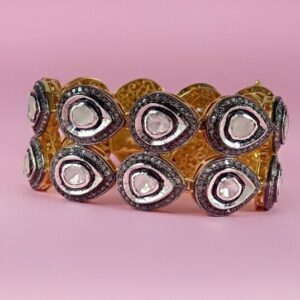 This image shows a silver bracelet adorned with multiple teardrop-shaped Polki diamonds, each surrounded by a pave setting of smaller diamonds. The bracelet has a luxurious and intricate design.