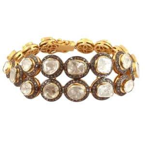 This image shows a gold-plated bracelet featuring two rows of uniquely shaped, uncut Polki diamonds. The warm gold setting enhances the natural sparkle of the diamonds, creating an elegant and traditional piece of jewelry. Pave Diamond Gemstone Bangle