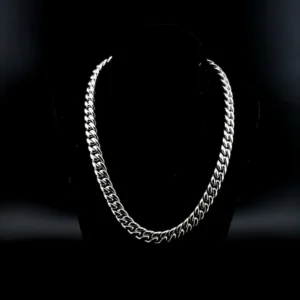 This image shows a sleek, polished silver Cuban link chain necklace displayed on a black velvet bust stand. The necklace has a thick, interlocking pattern typical of Cuban links, giving it a bold and luxurious appearance. The contrast between the bright silver and the dark background highlights the necklace's shine and craftsmanship, creating a strong, stylish, and elegant visual impact.