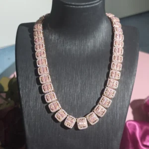 This image shows a luxurious hip-hop style necklace displayed on a black jewelry stand. The necklace is made up of large, square-shaped links, each encrusted with sparkling pink stones and bordered with clear stones, giving it a bold, iced-out appearance. The metal base appears to be 925 sterling silver, providing a high-end, polished backdrop for the vibrant stones. The necklace catches the light beautifully, highlighting its intricate craftsmanship and glamorous design. The overall presentation suggests elegance with a strong, fashionable statement.