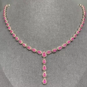 The image shows a short necklace featuring numerous teardrop-shaped, vibrant ruby red gemstones set in a likely gold or gold-toned frame. The necklace has a symmetrical design with a central pendant that cascades with additional ruby red stones. The background is a plain gray surface, highlighting the jewelry.